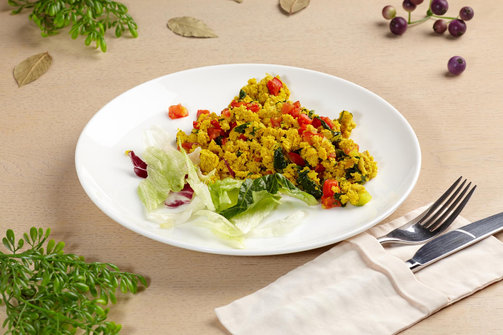 Tofu scramble with vegetables in a white plate on a wooden table.