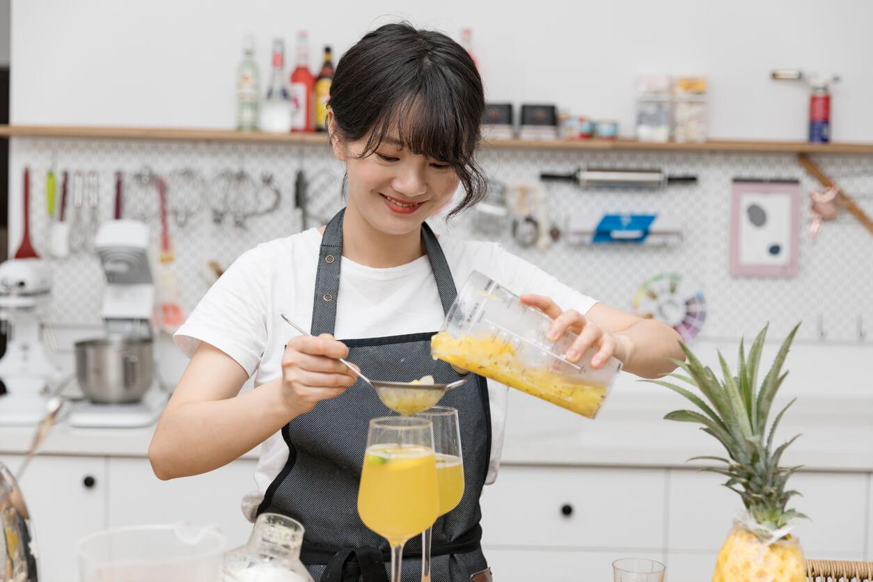 a smiling young chinese female pouring filtered juice into a glass in her kitchen