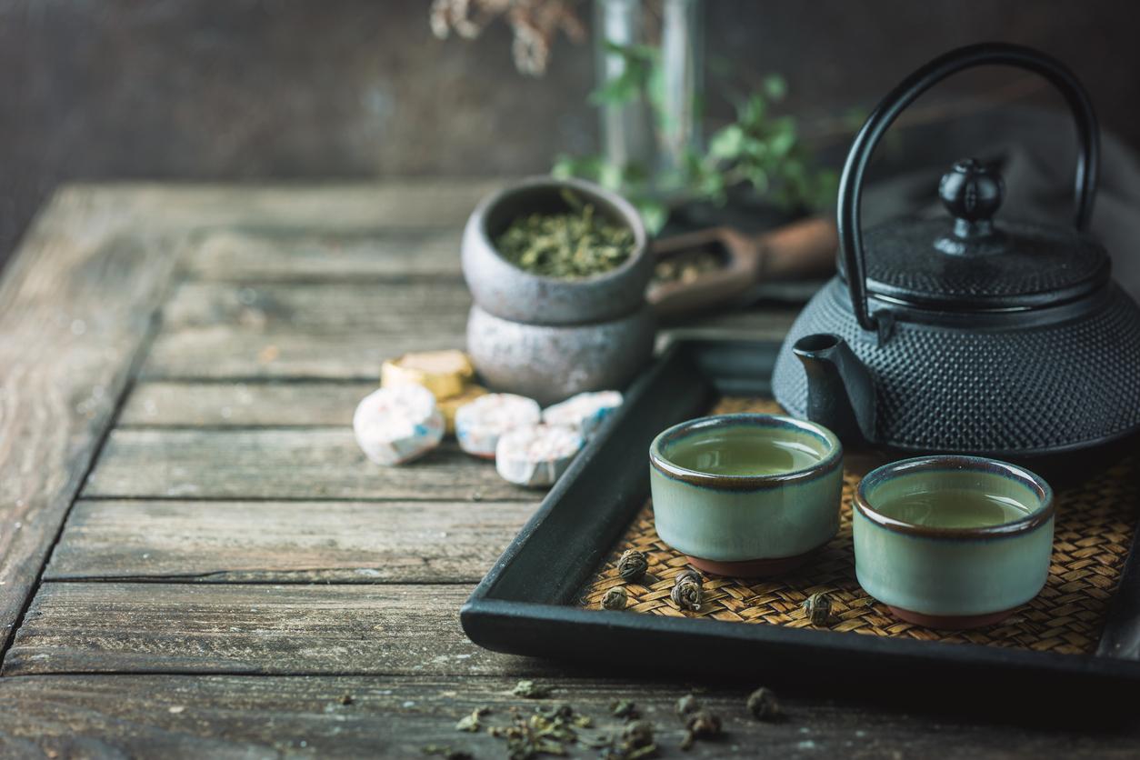 Still-life of japanese healthy green tea in a small cups and teapot over dark background