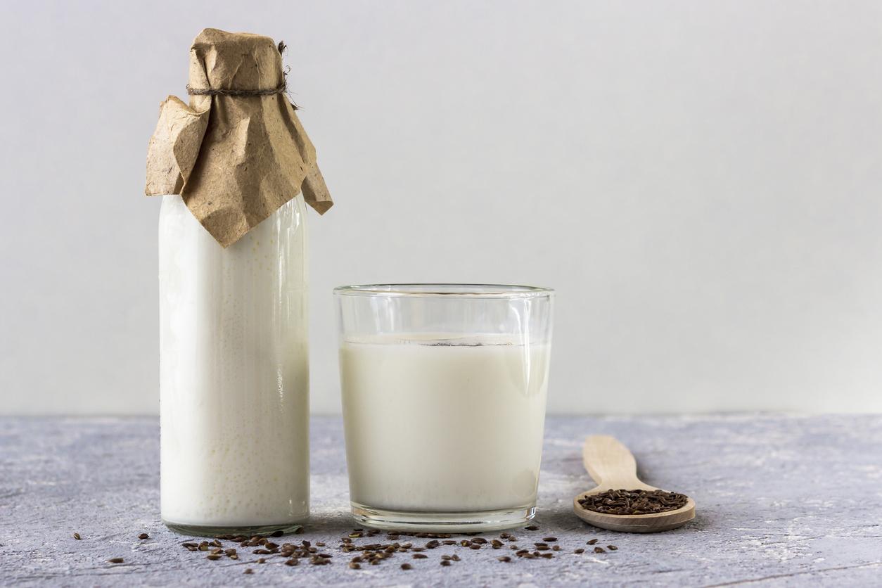 Glass bottle and glass of yogurt with flax seeds, wooden spoon with flax seeds on grey background.