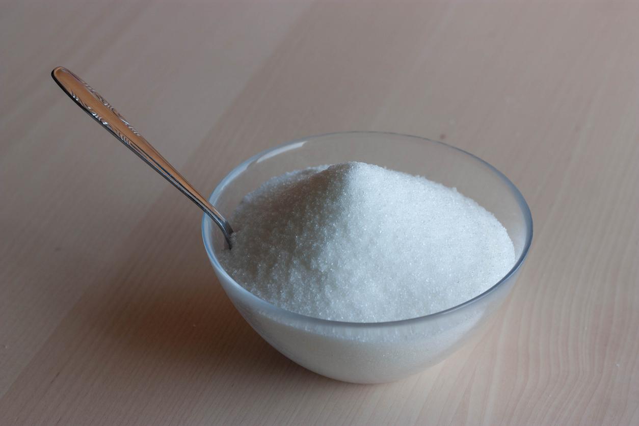 Glass jar with sugar and metal spoon on wooden bottom