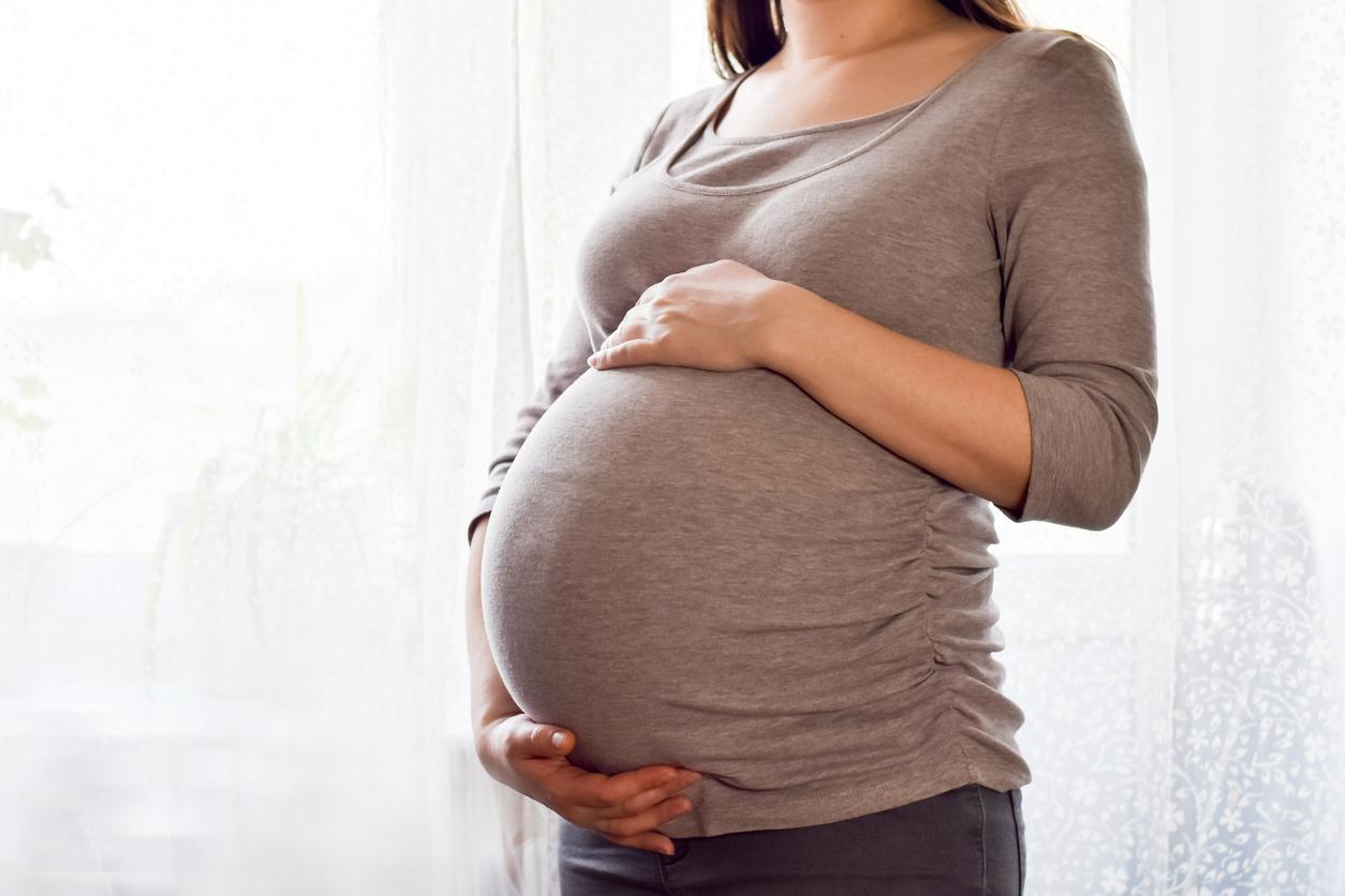 Pregnant woman with big belly at window. Maternity prenatal care and woman pregnancy concept. Young pregnant woman holds her hands on her swollen belly. Love concept. Horizontal with copy space.