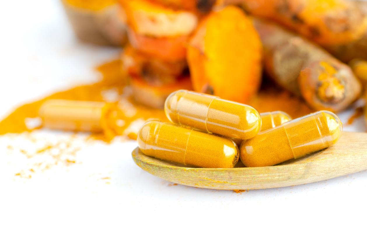 Closed up dry organic turmeric powder in capsule on wooden spoon on white background