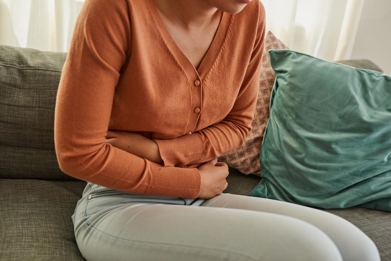 Shot of a woman experiencing stomach pain while lying on the sofa at home