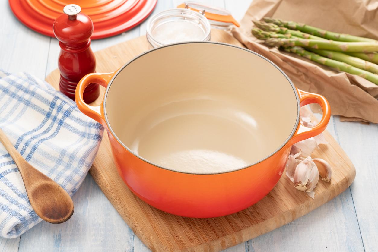 Orange dutch oven on wooden board with ingredients around it