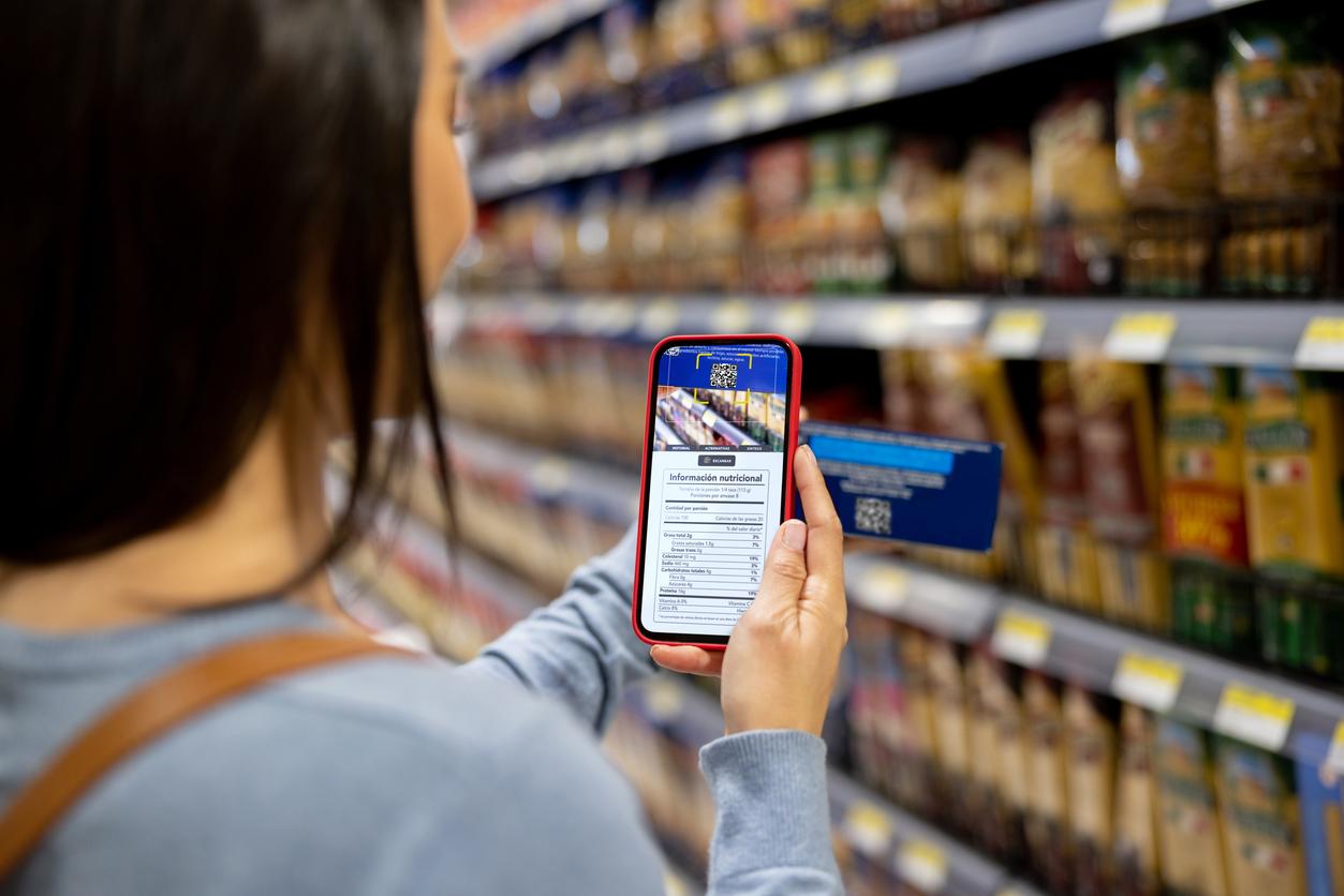 Close-up on a woman shopping at the supermarket and scanning a product label with her cell phone â healthy eating concepts
