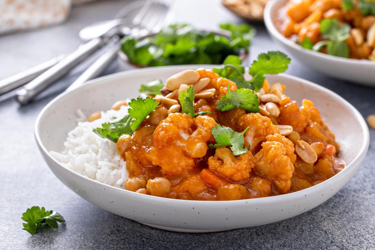 Vegan curry with cauliflower, chickpeas and butternut squash topped with peanuts, served with rice and cilantro