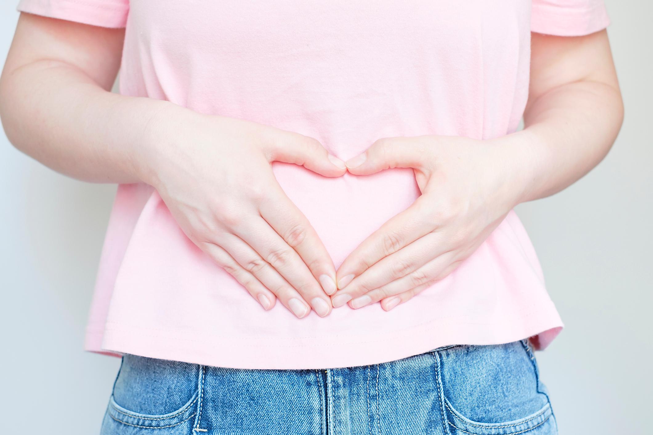 Female hands in the shape of a heart on the stomach, concept of female health.
