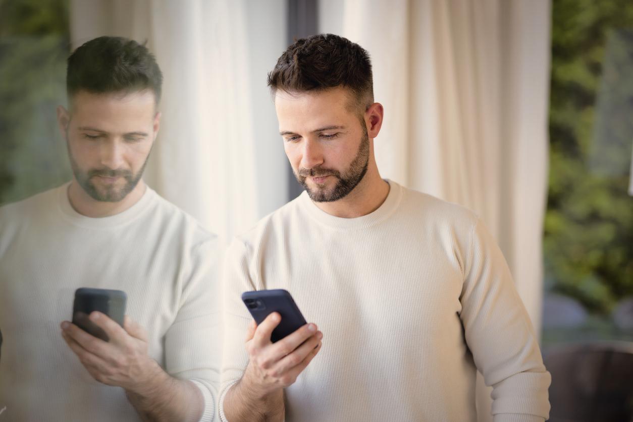 A serious face man standing at the window and using mobile phone. Confident male making a phone call.