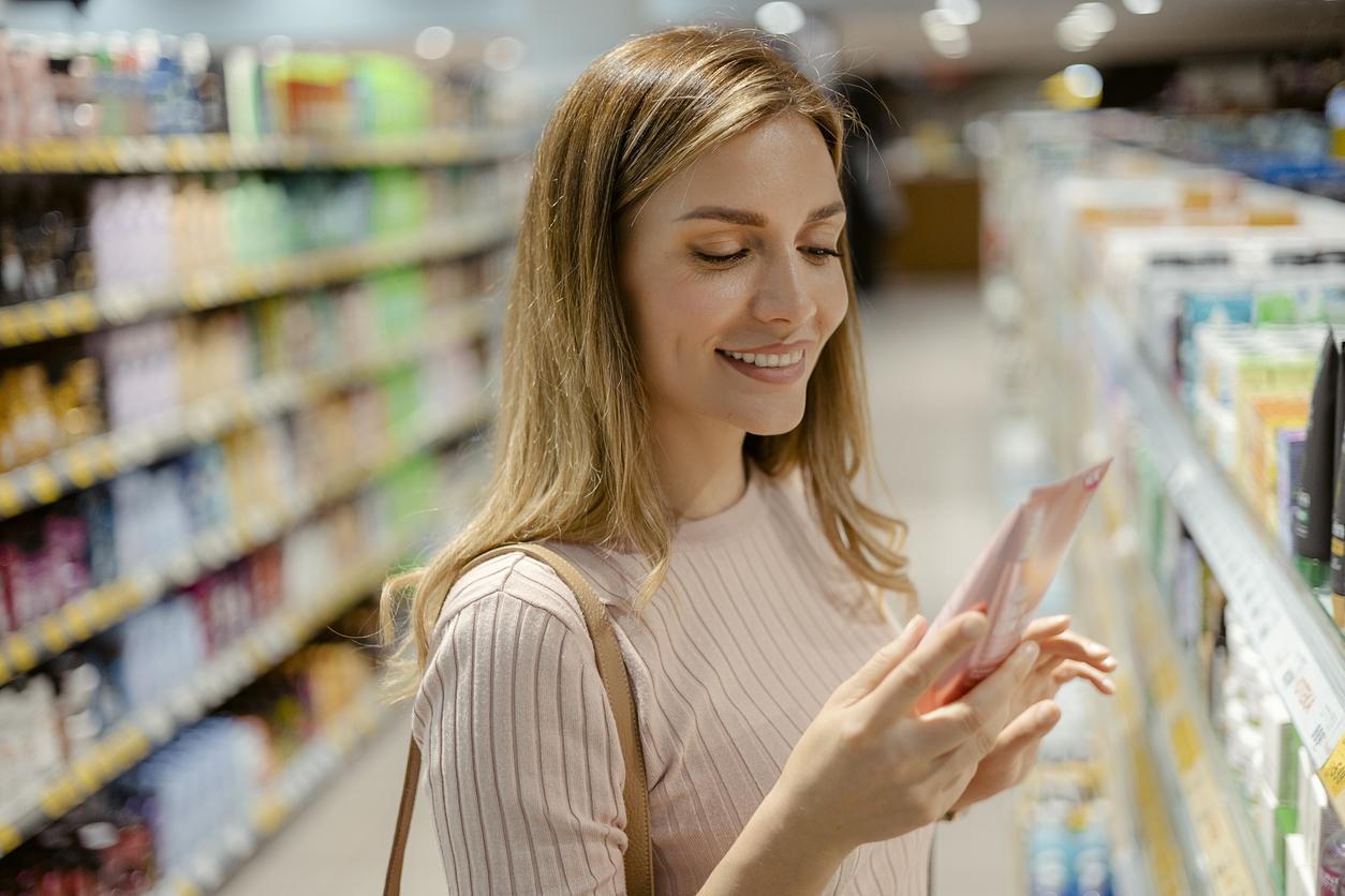 Young woman reading ingredients of skin care product while shopping at the store. Personal care and modern cosmetology