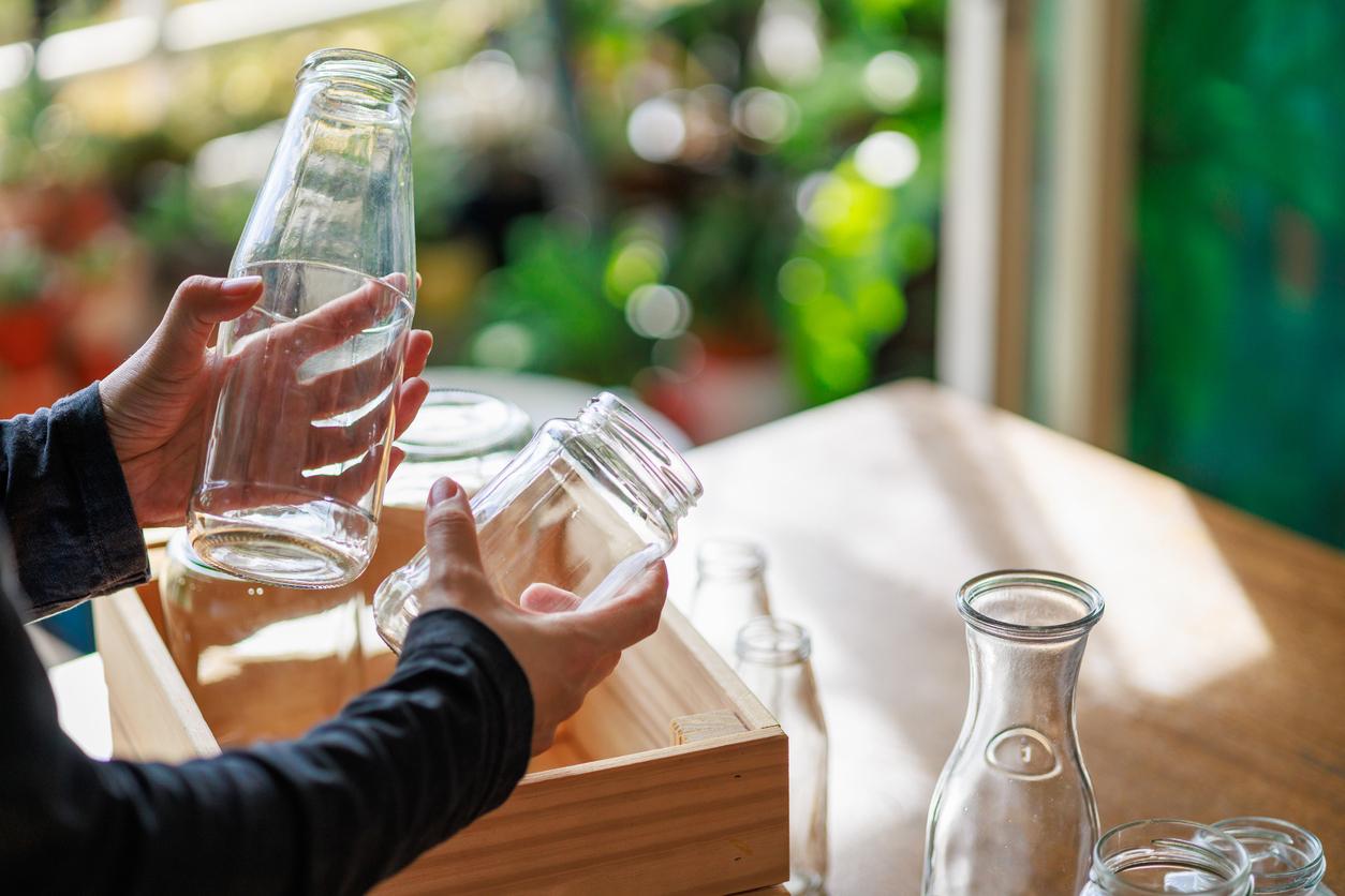 Cropped image of an Asian woman's hands placing empty glass jars into a wooden box, ready for recycling, showcasing a sustainable lifestyle.