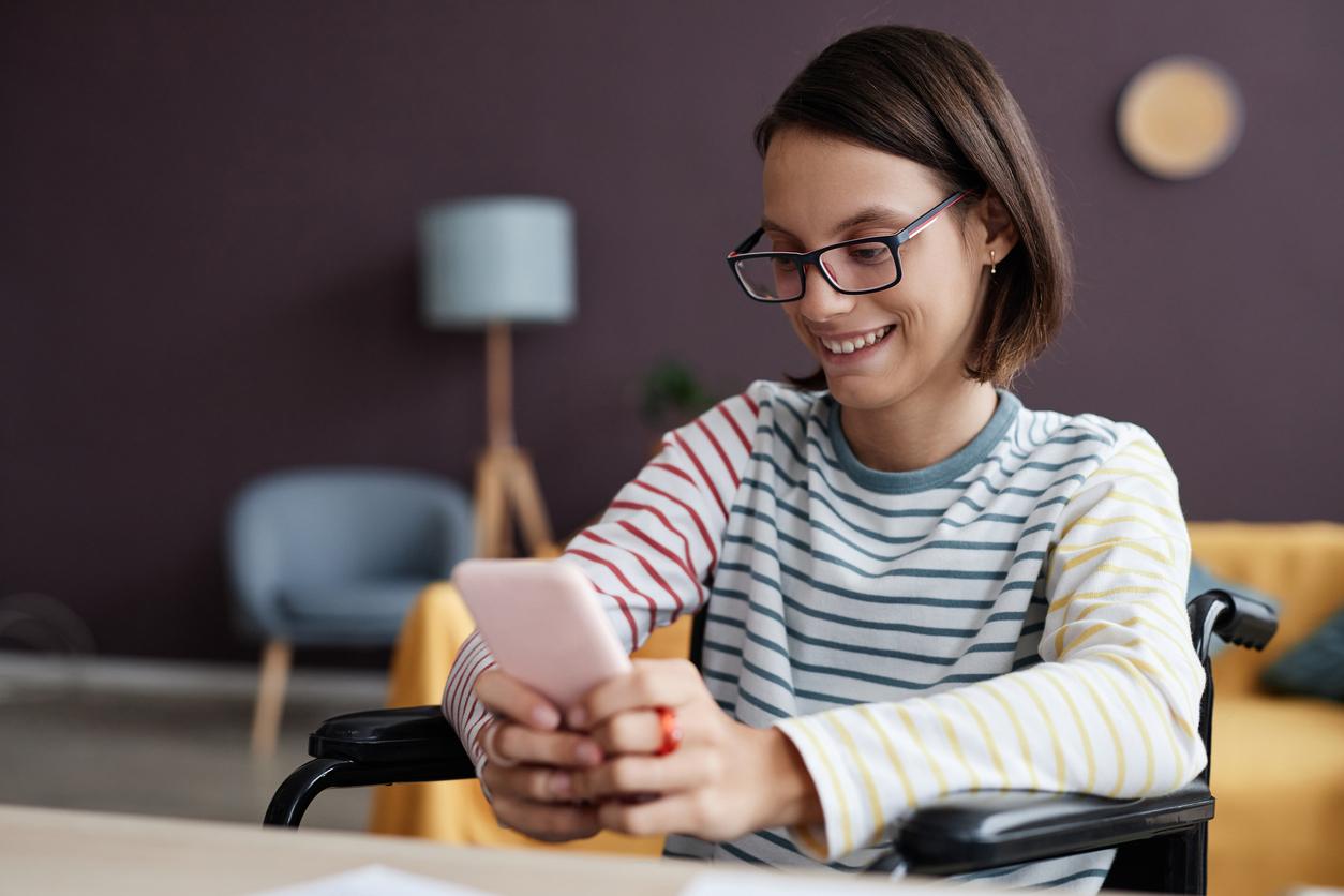 Portrait of smiling teenage girl with disability using smartphone at home while browsing social media, copy space