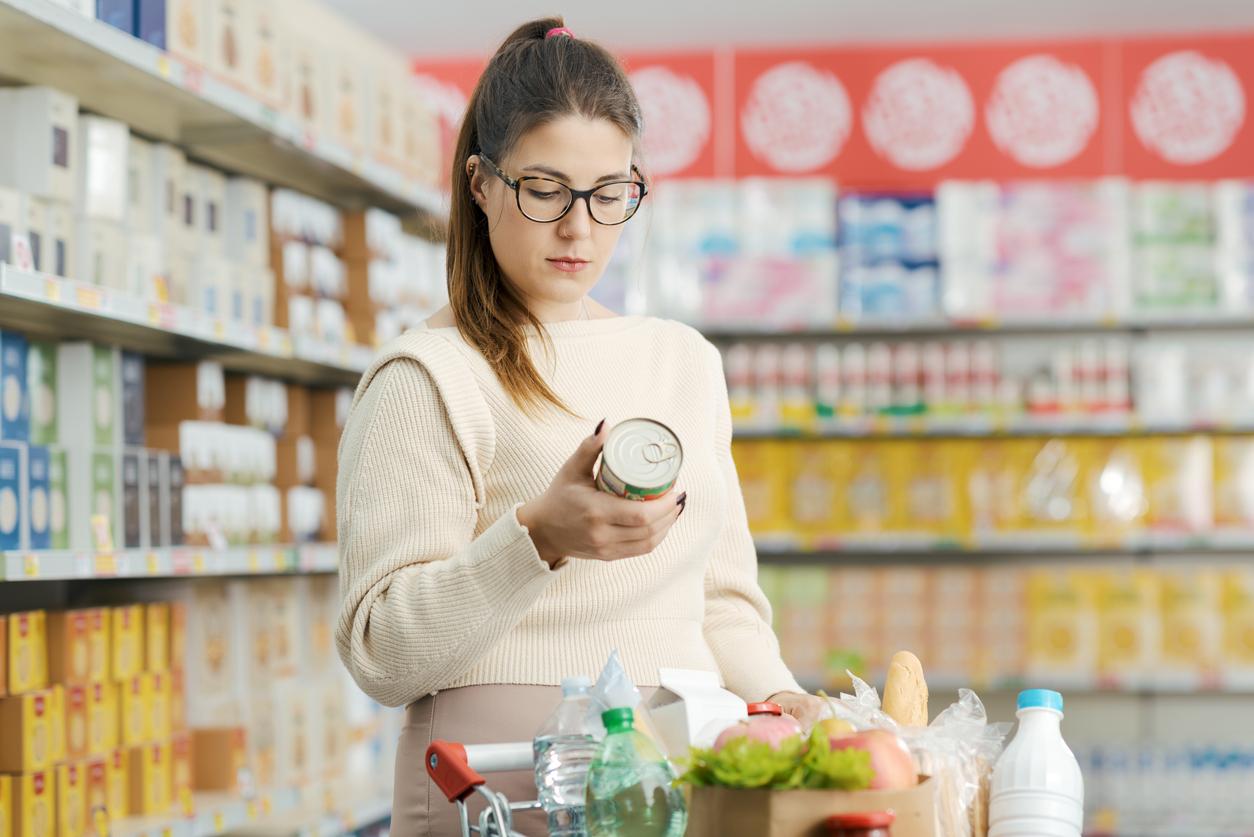Woman buying groceries at the supermarket, she is holding a can and checking the food label