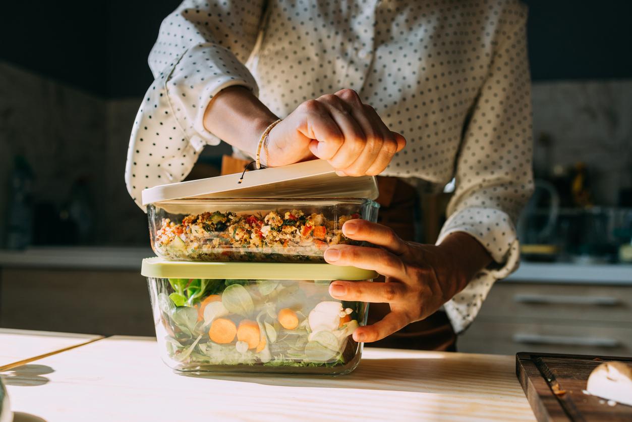 A person prepping healthy meals, carefully sealing nutritious food in stacks of transparent containers on a well-lit kitchen counter.