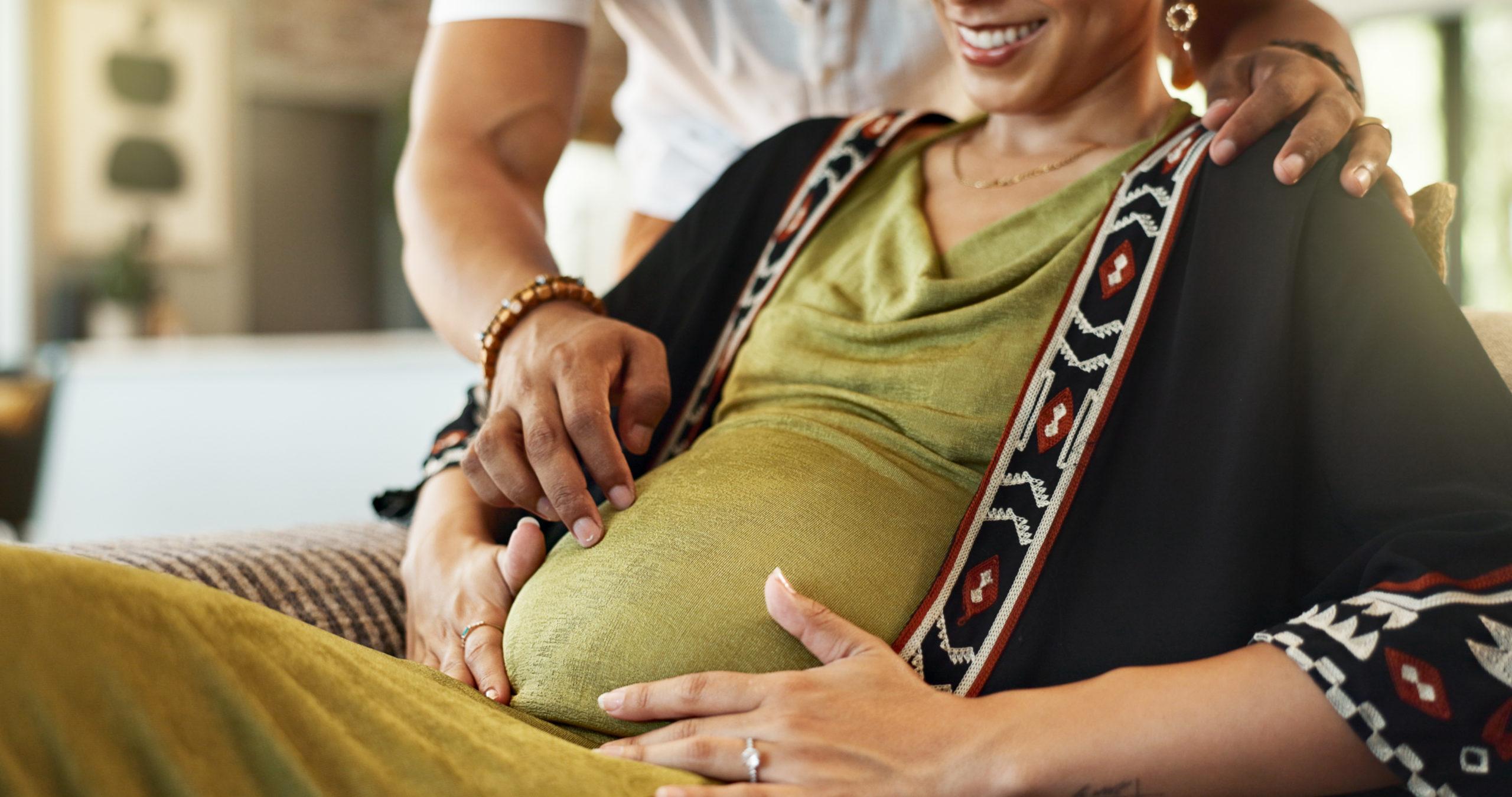 Pregnant, couple and hands on tummy on sofa with bonding, stomach touch and support with maternity and motherhood. Future parents and affection on couch with healthy pregnancy and excited for baby