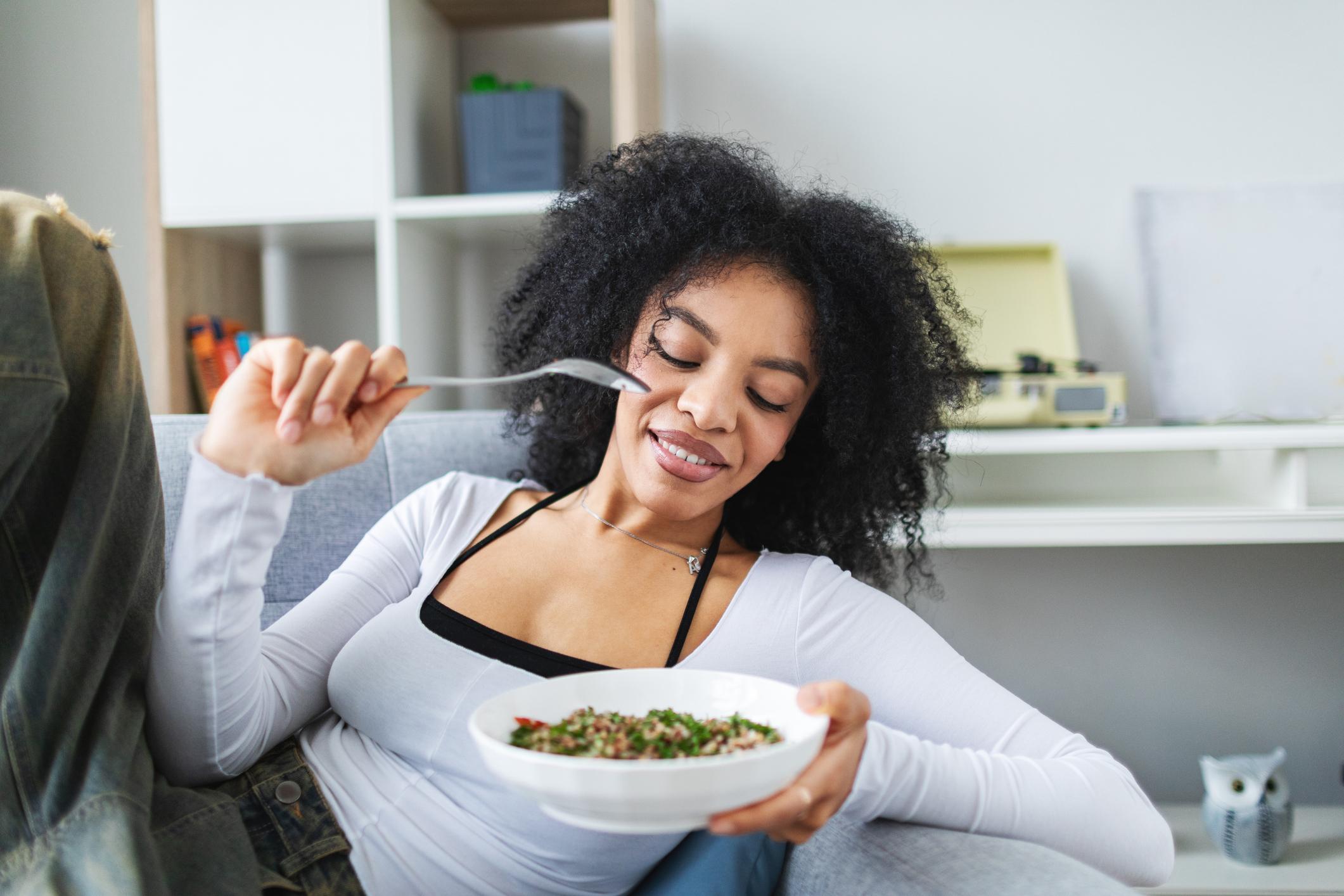 Young adult woman relaxing at home, sitting in the chair and eating