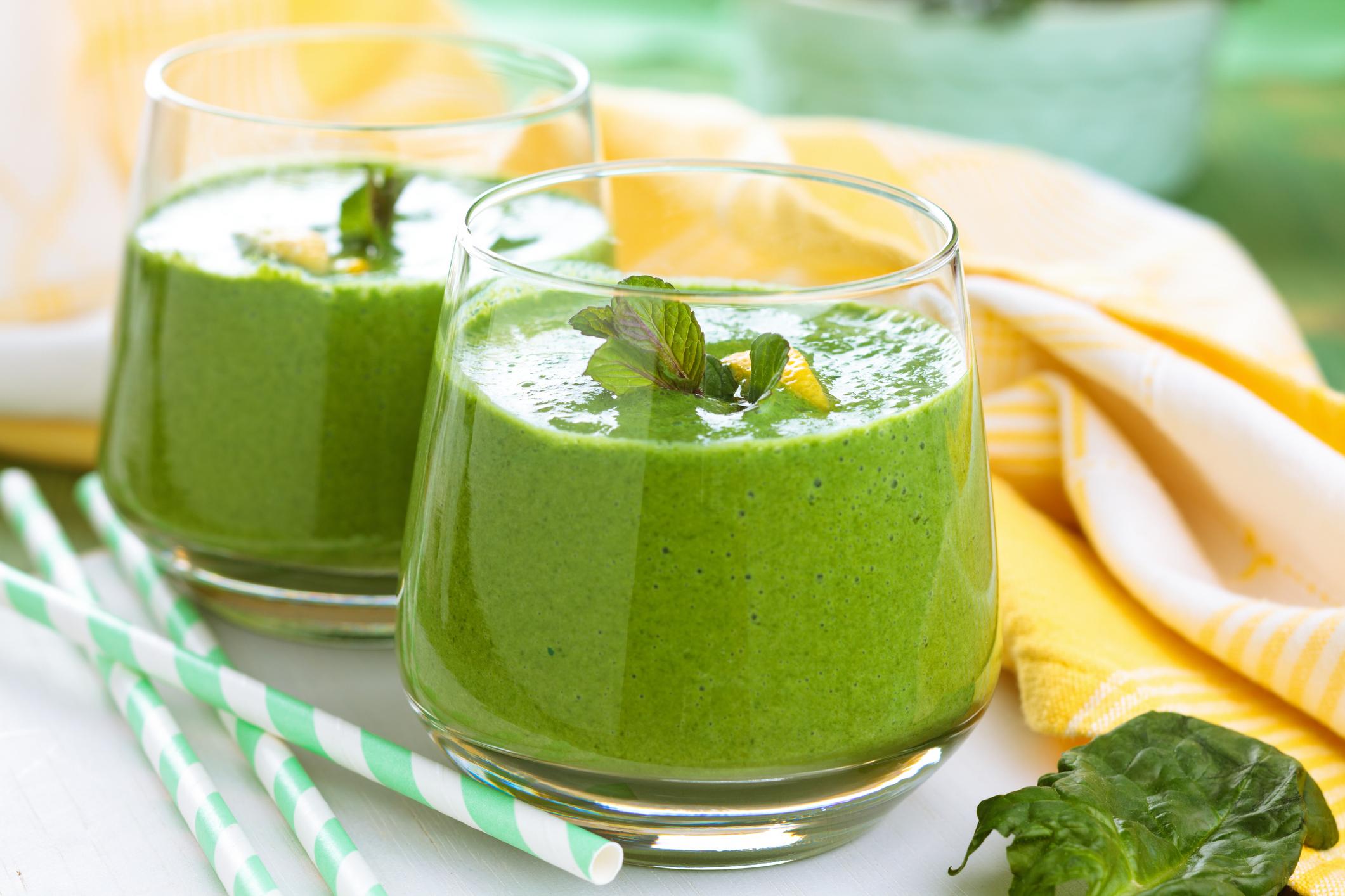 Spinach smoothie with mint leaves and lemon on table.
