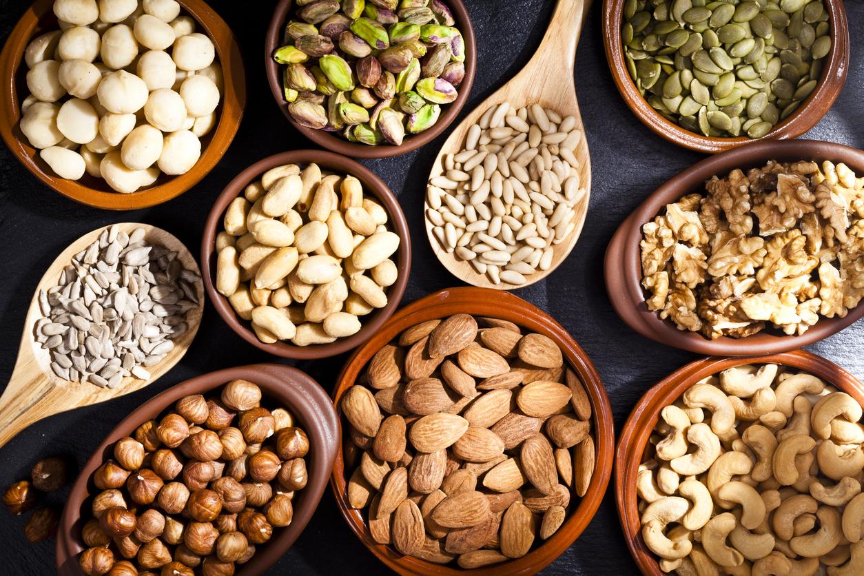Top view of a rustic wood table filled with a large assortment of nuts like pistachios, hazelnut, pine nut, almonds, pumpkin seeds, peanuts, cashew and walnuts. Some nuts are in brown bowls and wooden spoon and others directly on the table. Predominant color is brown. DSRL studio photo taken with Canon EOS 5D Mk II and Canon EF 100mm f/2.8L Macro IS USM