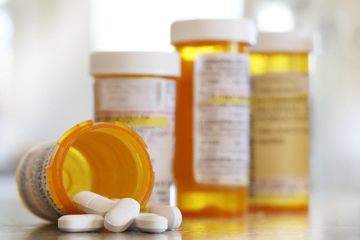 Pills pour out of a prescription medication bottle onto a kitchen counter.  Several other pill bottles stand out of focus in the background.