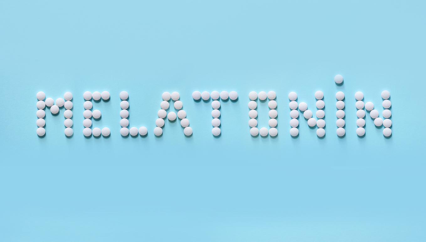 Melatonin, the word is laid out on a blue background of tablets. Tablets, hormone and excipients to improve sleep.