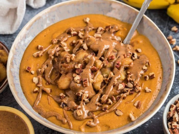 a bowl of pumpkin puree topped with chopped pecans and a drizzle of nut butter