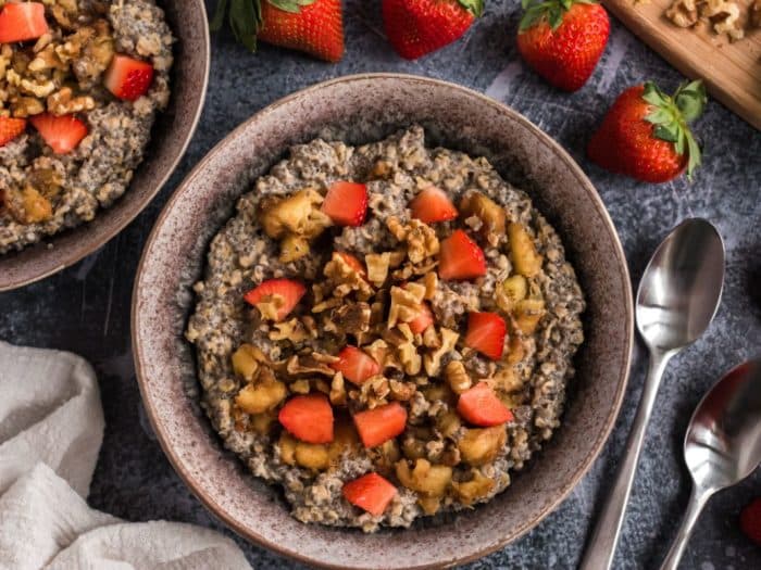 two bowls of a dark-colored porridge or oatmeal topped with sliced strawberries and chopped walnuts